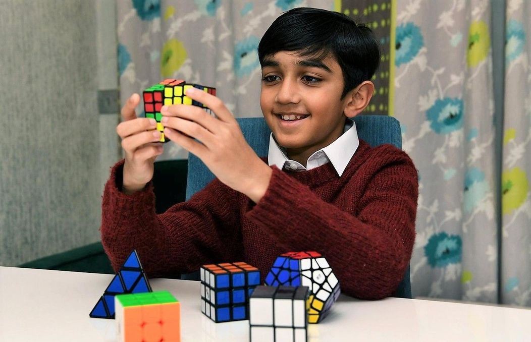 Yusuf Shah zâmbește în timp ce rezolvă un cub Rubik, una dintre jucăriile lui favorite