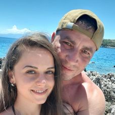 Marian Godină și soția sa zâmbesc în fața camerei de fotografiat, pe o plajă, în vacanța de vară din 2021