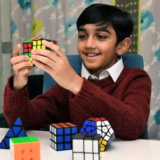 Yusuf Shah zâmbește în timp ce rezolvă un cub Rubik, una dintre jucăriile lui favorite